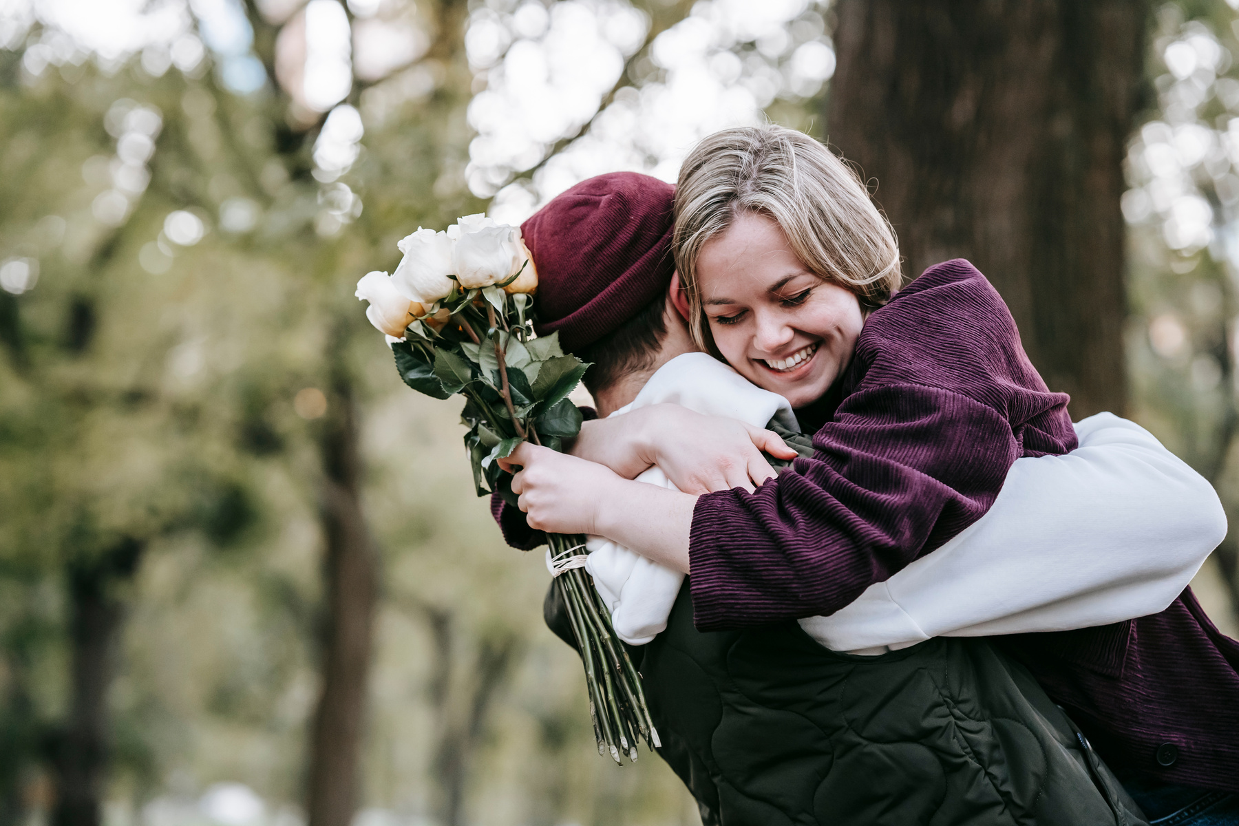 Smiling loving girlfriend with white roses hugging boyfriend in hat